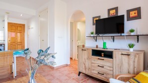Een moderne woonkamer met een houten kast, een aan de muur bevestigde televisie en een eethoek met een tafel en stoelen.