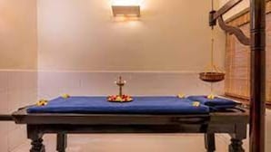 A room with a massage table, a small altar with flowers, and a hanging light fixture. - Capital Plaza Residency (Mannarkkad)