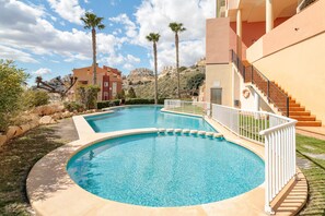 Una piscina con barandilla blanca, rodeada de follaje y palmeras, con edificios al fondo.