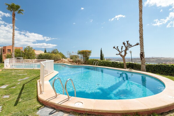 Piscina com vista para o mar, cercada por palmeiras e um muro branco.