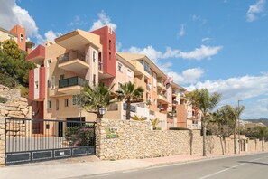 Um edifício residencial de vários andares com varandas, uma parede de pedra e céu claro.
