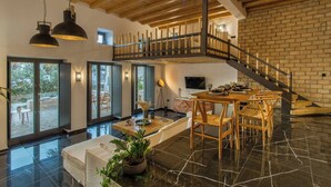 A spacious living area with a high ceiling, a wooden staircase, and a dining area with a table and chairs.