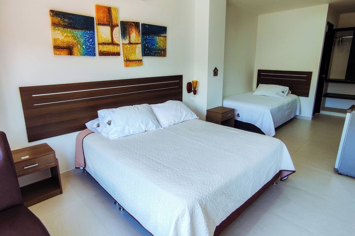 Ein Hotelzimmer mit zwei Betten, einem Holzkopfende, einer Wand-Klimaanlage und einer Reihe abstrakter Gemälde.