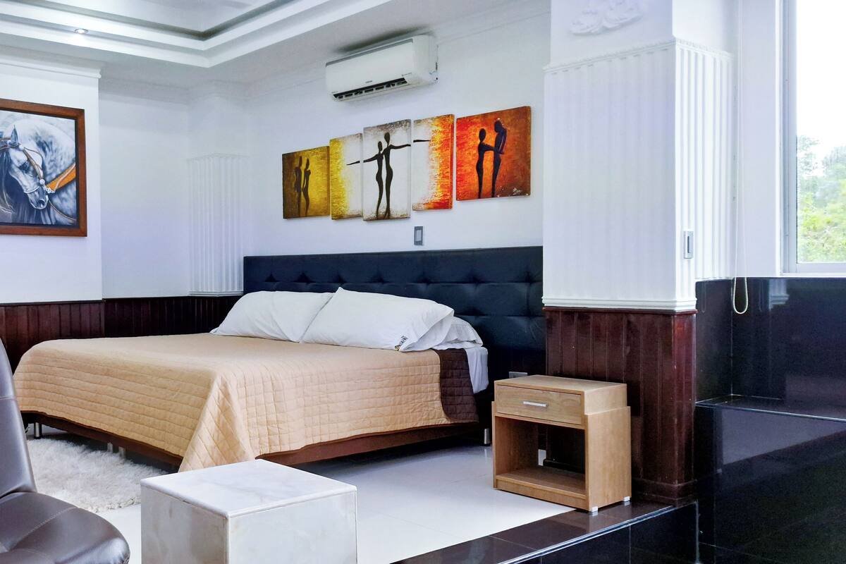 Ein modernes Schlafzimmer mit einem großen Bett, einem Sessel, einem Nachttisch und einem Bild an der Wand.