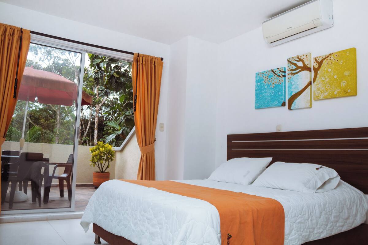 Ein Schlafzimmer mit einem Bett, einer Topfpflanze, einer Glastür zum Balkon und einer Wand-Klimaanlage.