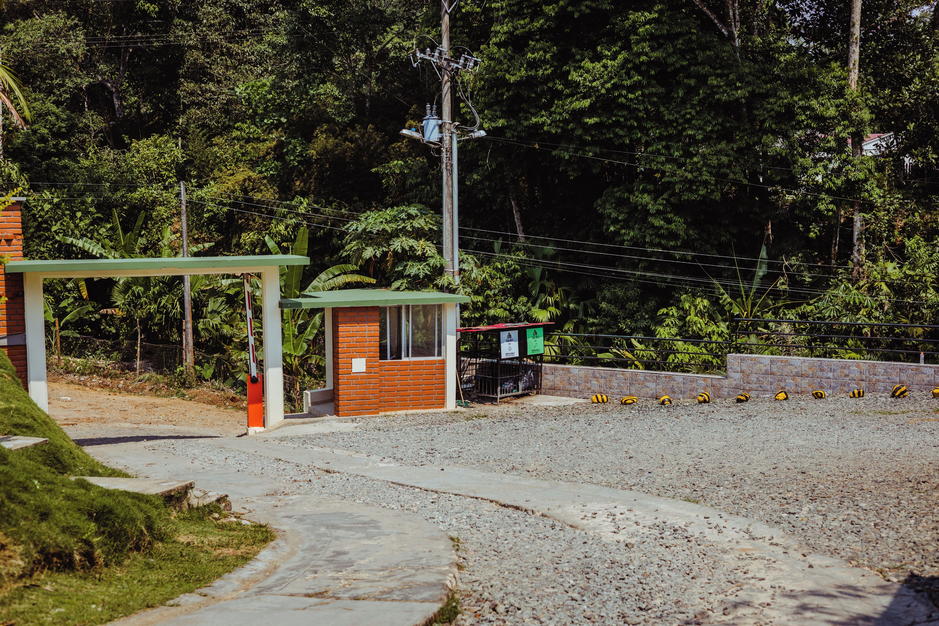 A small building with a green roof, a brick wall, and a gravel path leading to it.