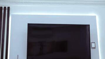 En moderne stue med et fladskærms-tv monteret på en hvid væg, en dekorativ vase og en indbygget reol med elektronisk udstyr.