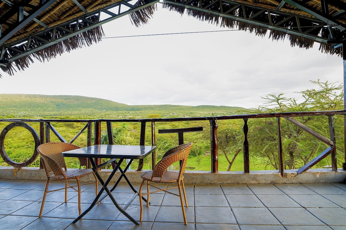A covered outdoor seating area with a table and chairs, overlooking a green landscape.