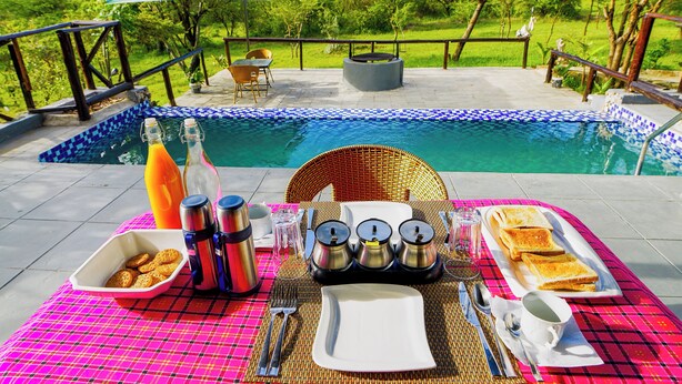 A dining setup with a table, chairs, and a poolside view. - Kitumo Mara Lodges  (Maasai Mara)