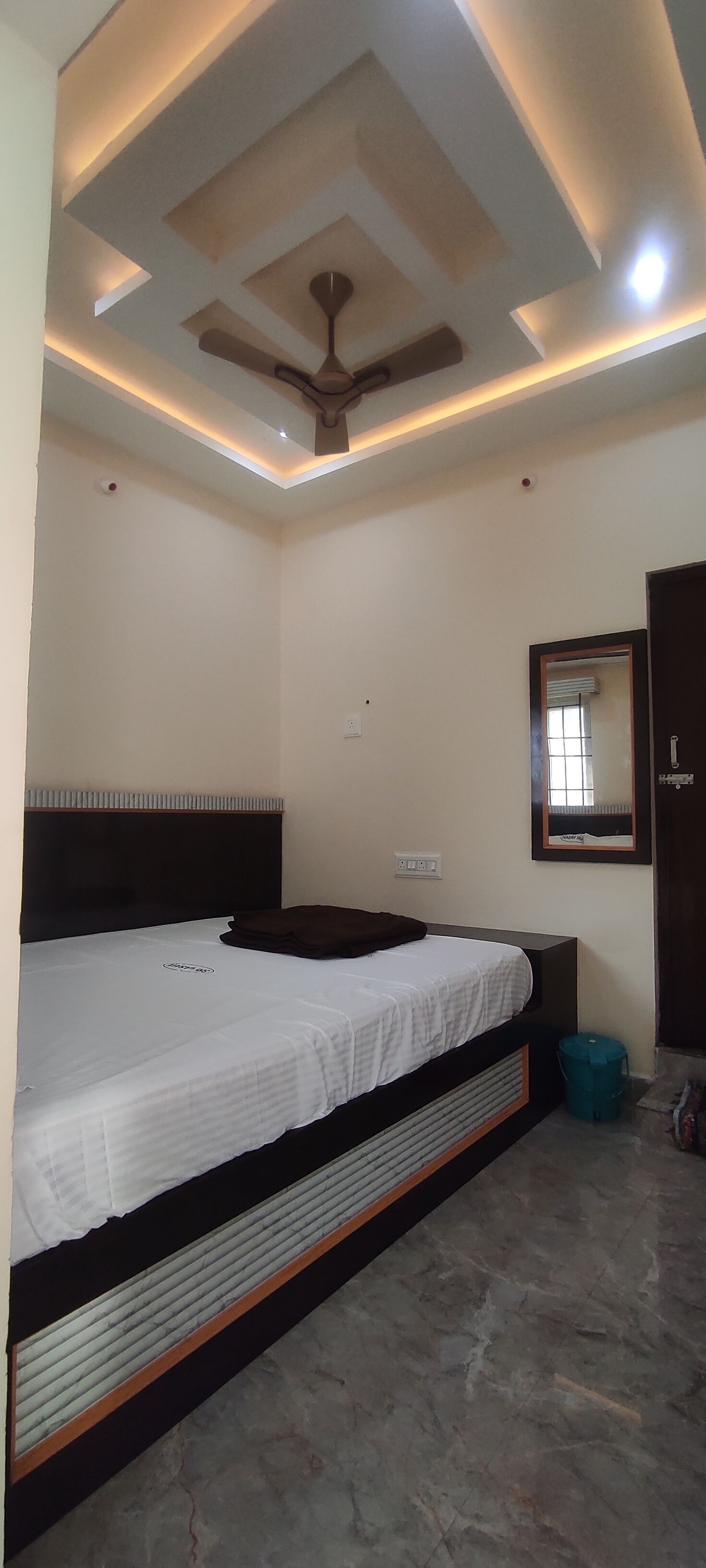 A bedroom with a bed, a ceiling fan, recessed lighting, a mirror, and a door.