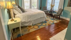 Un dormitorio con cama, mesitas de noche, una silla, una mesa y un ventilador de techo.
