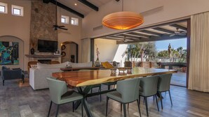 A spacious living area with a large wooden dining table, comfortable seating, a fireplace, and a view of the outdoors.