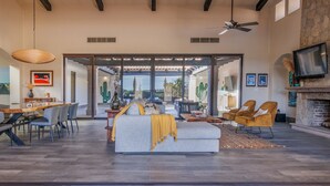 A spacious living area with a large sofa, dining table, and chairs, a fireplace, and a television.