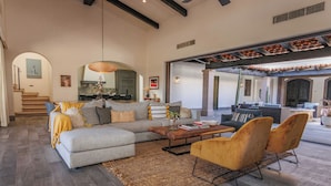 A spacious living area with a grey sofa, yellow armchairs, and a coffee table. A kitchen is visible in the background, and there is a staircase leading to another level.