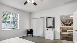 Ein Schlafzimmer mit Bett, Kommode, Stuhl und einem Fenster mit Jalousien.