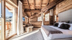 Un dormitorio de cabaña de madera con una cama grande, una mesita pequeña y una silla.