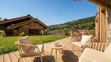 Eine Holzterrasse mit Sitzgelegenheiten im Freien, ein rustikales Gebäude und Blick auf ein grünes Tal.