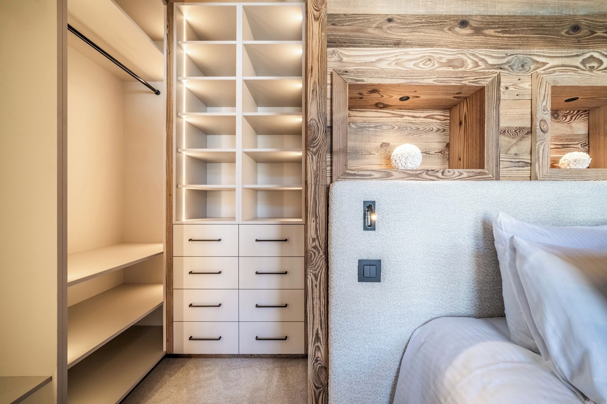 A bedroom with a bed, a wooden headboard, and a built-in wardrobe with multiple shelves and drawers.