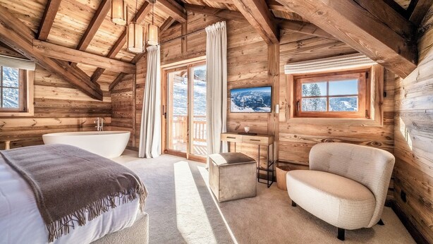 Un dormitorio de cabaña de madera acogedor, con un ventanal grande, una bañera y un sillón cómodo.
