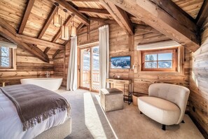 Een gezellig houten slaapkamer met een groot raam, een badkuip en een comfortabele fauteuil.