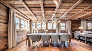 Un interior de madera con una mesa y sillas de comedor, ventanas amplias y una araña.