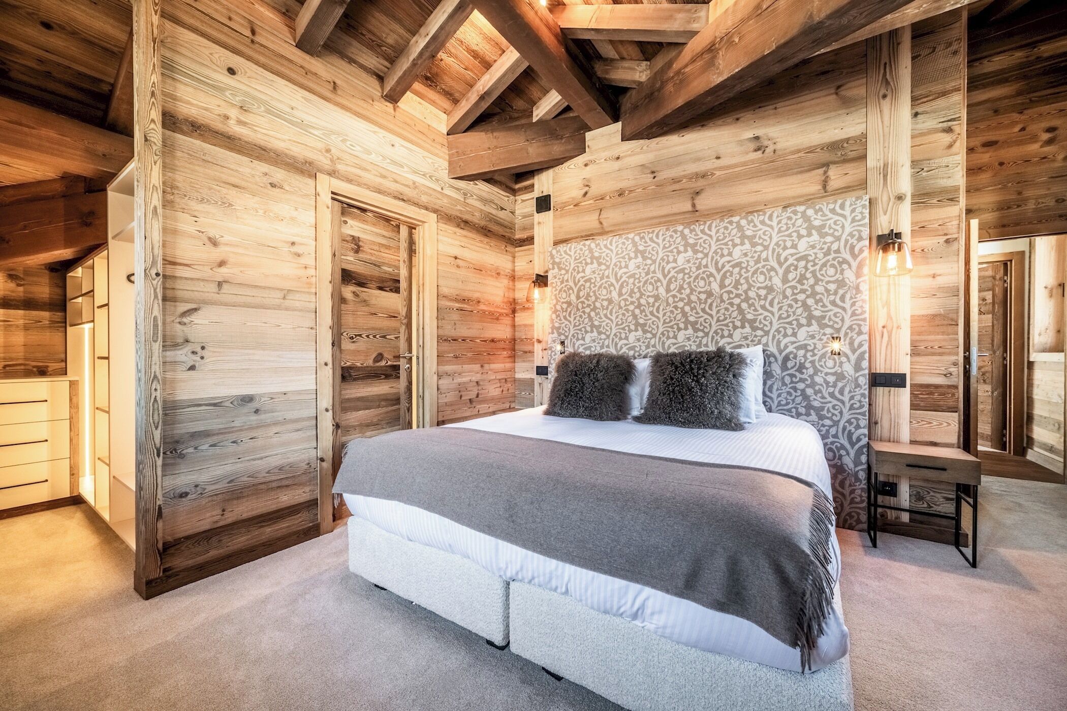 A wooden cabin bedroom with a bed, a nightstand, and a patterned wall.