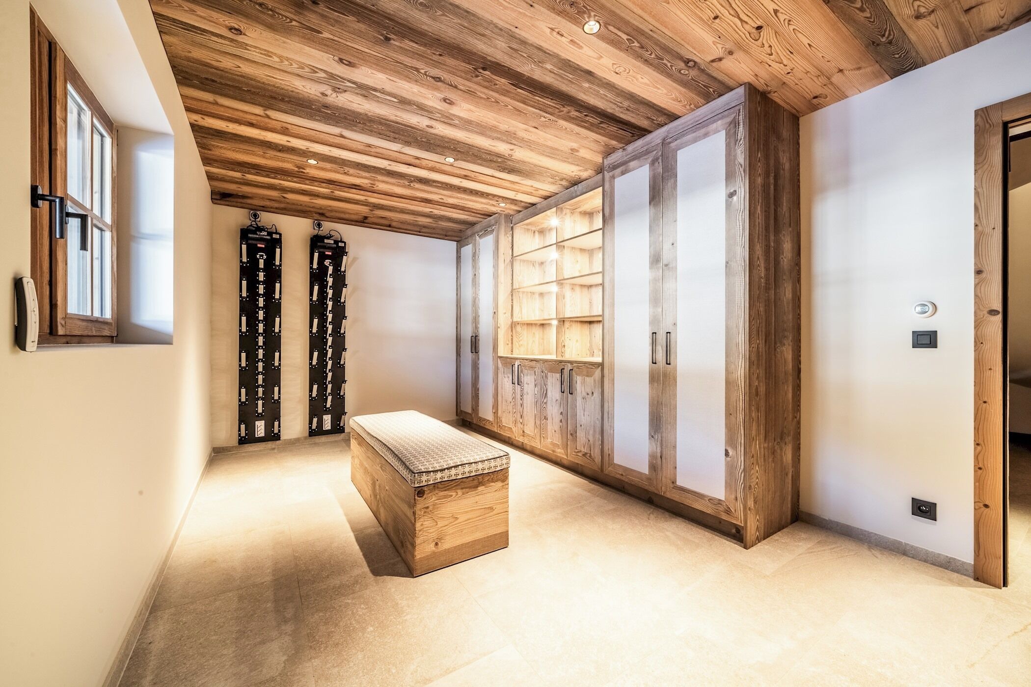 Un couloir avec un plafond en bois et des placards, un banc et une porte dotée d’une poignée.
