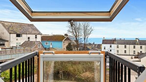 Une vue depuis un balcon doté d’une lucarne, donnant sur un quartier résidentiel avec des maisons et une étendue d’eau.