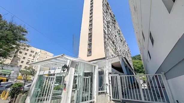 Un edificio alto con fachada moderna, estructura de vidrio con estructura metálica y una entrada protegida por una reja.