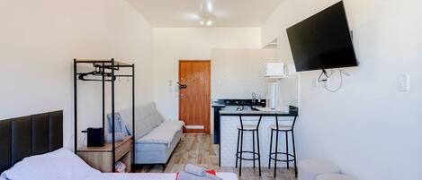 Een hotelkamer met een bed, een kleine kitchenette, een aan de muur bevestigde televisie en een deur die naar een andere kamer leidt.