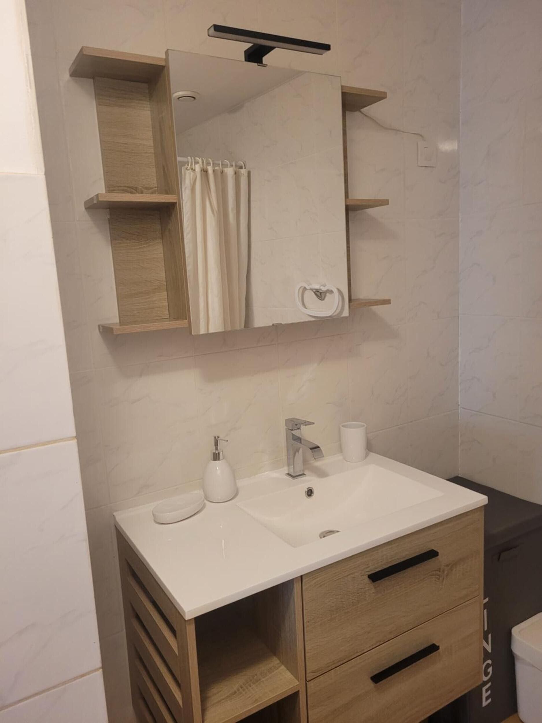 Een badkamer met een witte wasbak, een spiegel, een handdoekhouder en een douchegordijn.