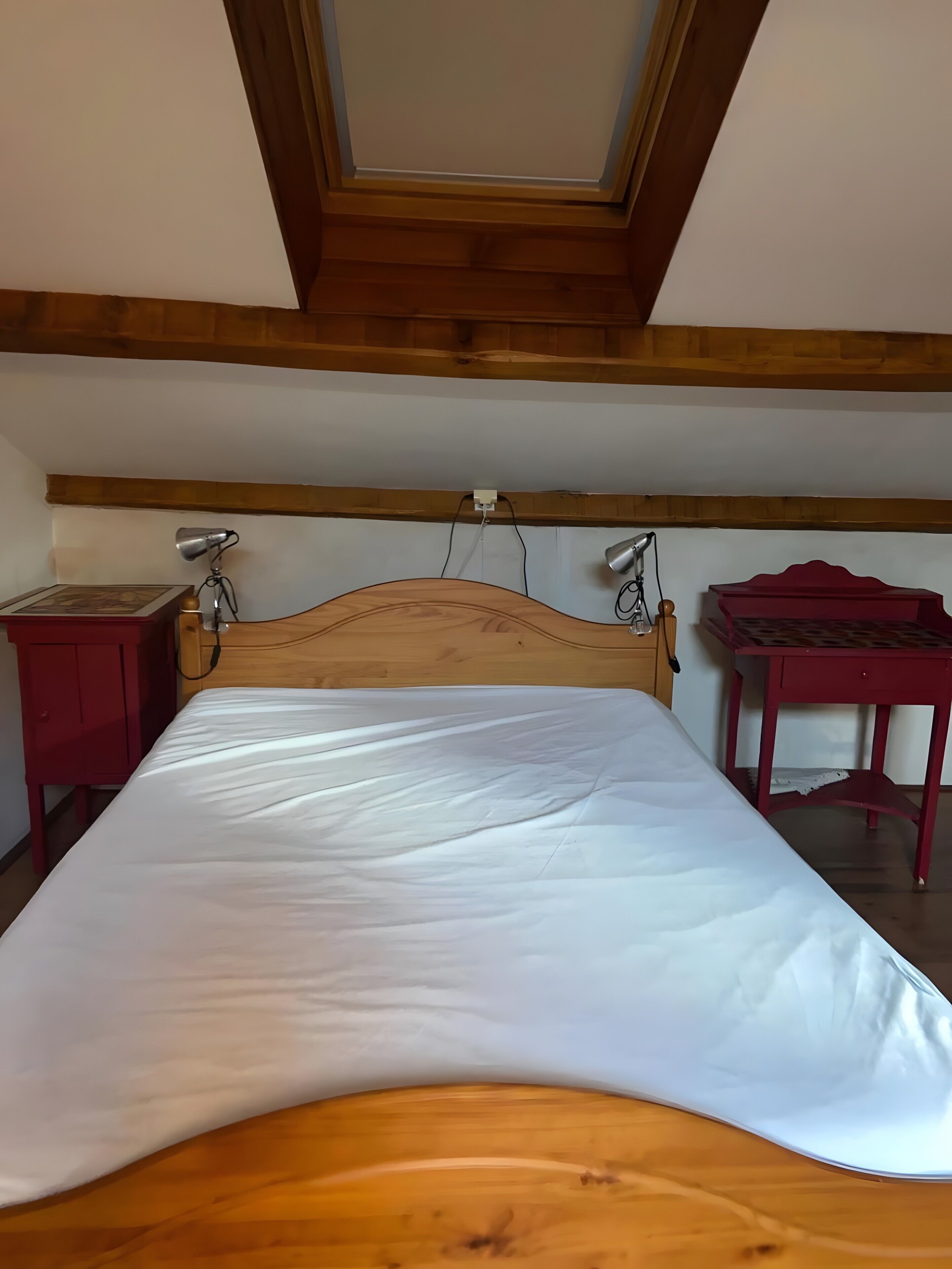 A room with a wooden bed, two bedside lamps, a red nightstand, and a red table.