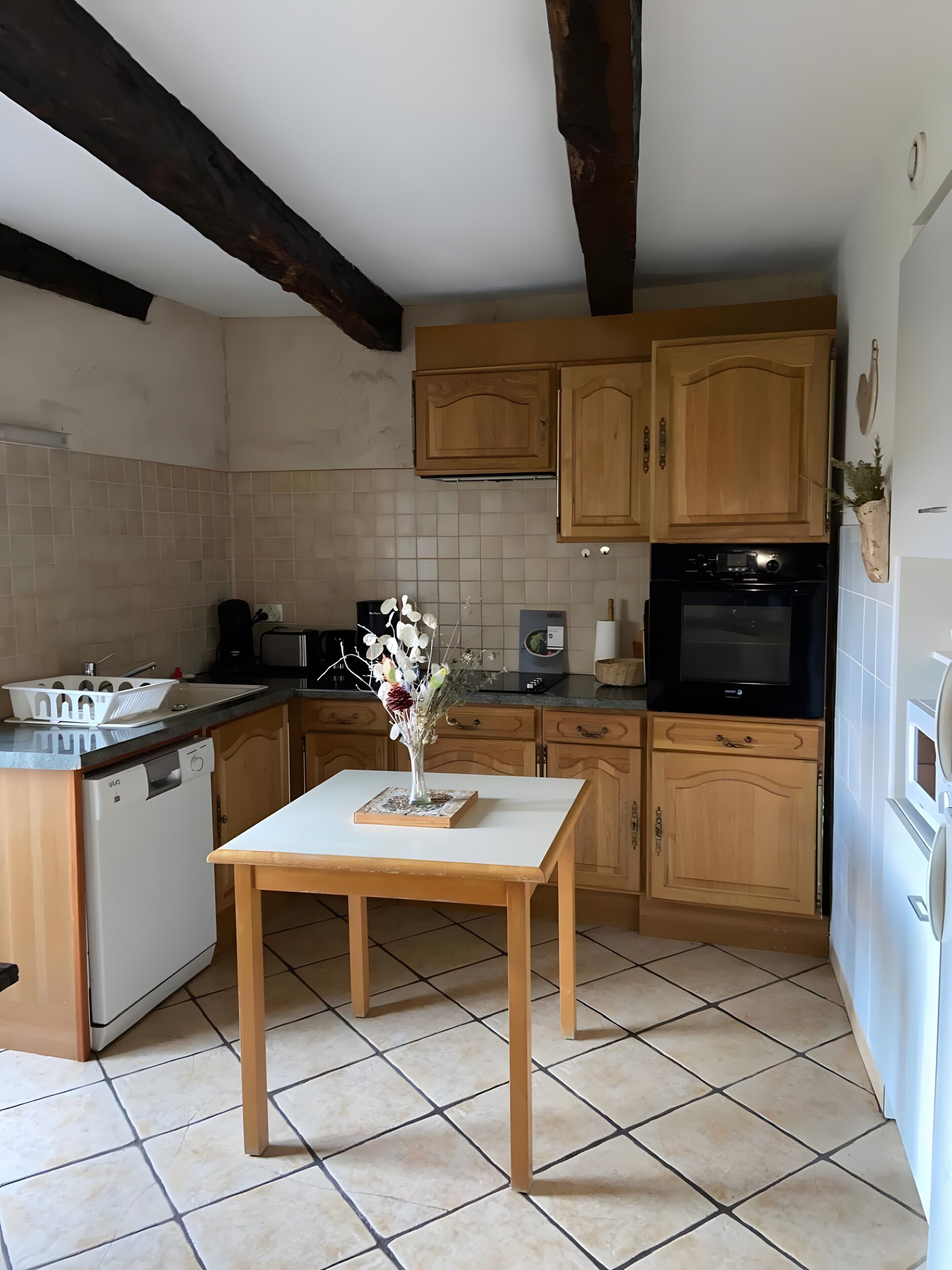 A kitchen with wooden cabinets, a dishwasher, a table with a vase, and a tiled floor.