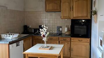A kitchen with wooden cabinets, a dishwasher, a table with a vase, and a tiled floor.