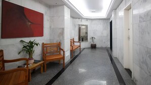 A hallway with marble walls, wooden benches, a red abstract painting, and a potted plant.