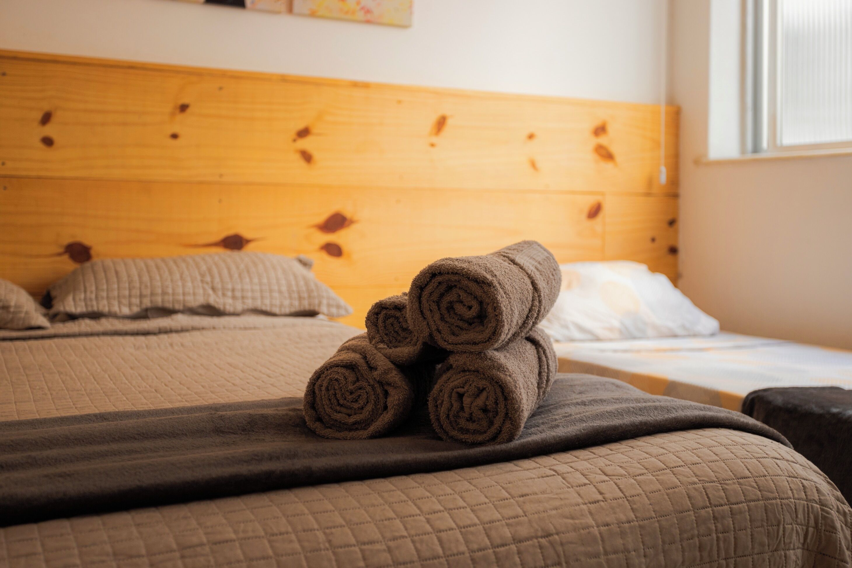 Un lit bien fait, avec une couverture matelassée, une tête de lit en bois et des serviettes enroulées posées sur le lit.