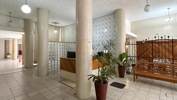 A spacious lobby with a reception desk, large columns, potted plants, and a wooden bench.