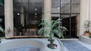A building entrance with a curved pathway, palm trees, and a decorative statue.