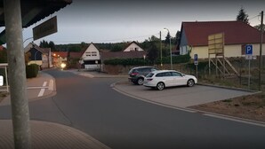 A street view with two parked cars, a building with a red roof, and a parking sign. - Gästehaus Zum Felsenkeller Steigerthal  (Nordhausen)