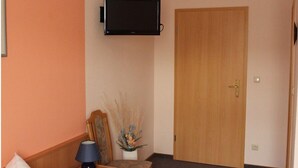A room with a wooden door, a mounted television, a chair, a table, and a vase with dried plants. - Gästehaus Zum Felsenkeller Steigerthal  (Nordhausen)