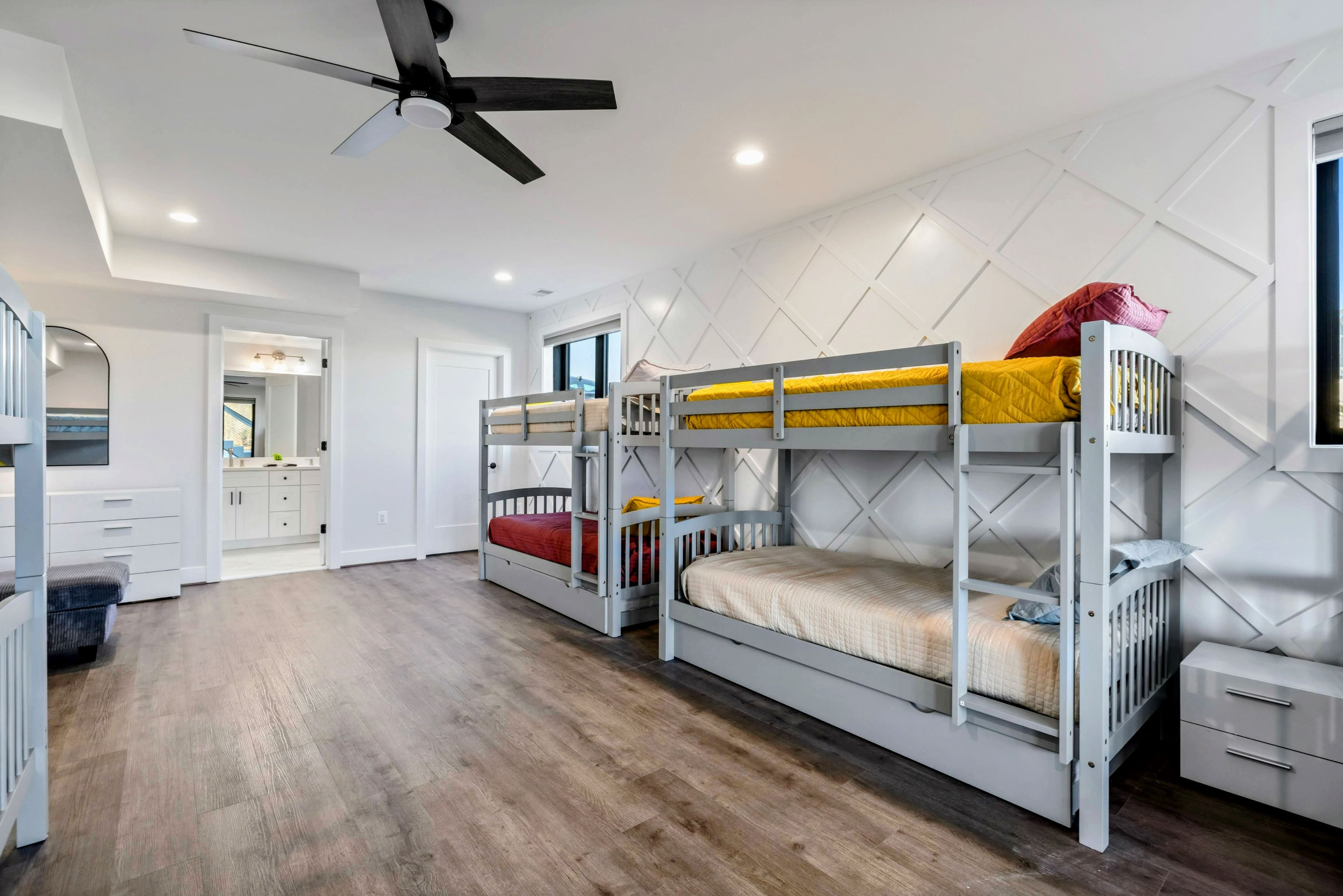 A room with bunk beds, a ceiling fan, and a kitchenette.