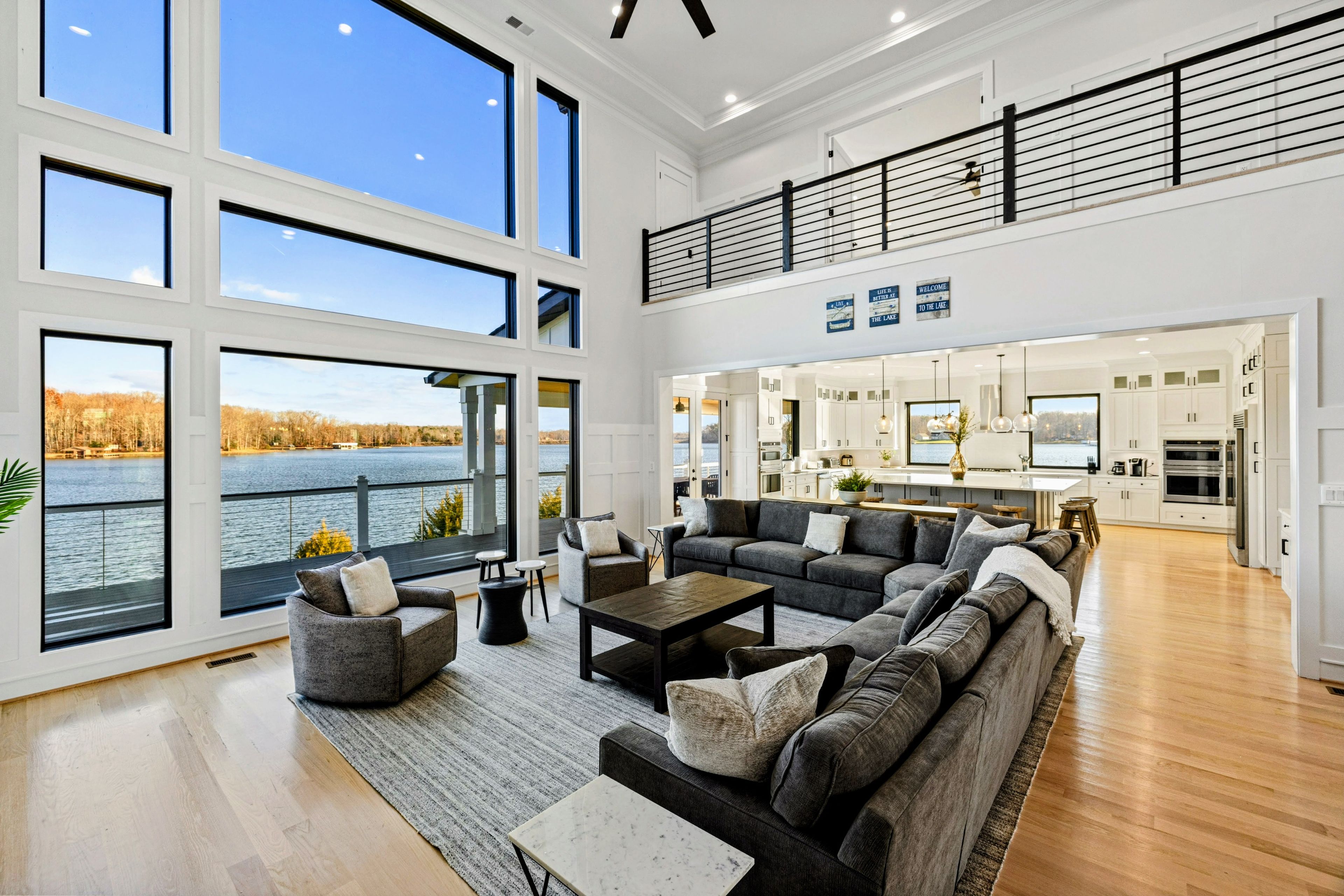 A spacious living room with a large sofa set, a coffee table, and a view of a lake through expansive windows.