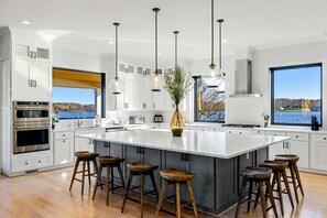 A modern kitchen with white cabinetry, a large island with stools, and a view of a body of water.