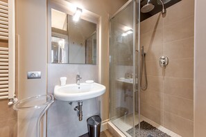 A bathroom with a glass shower enclosure, a sink, and a mirror.