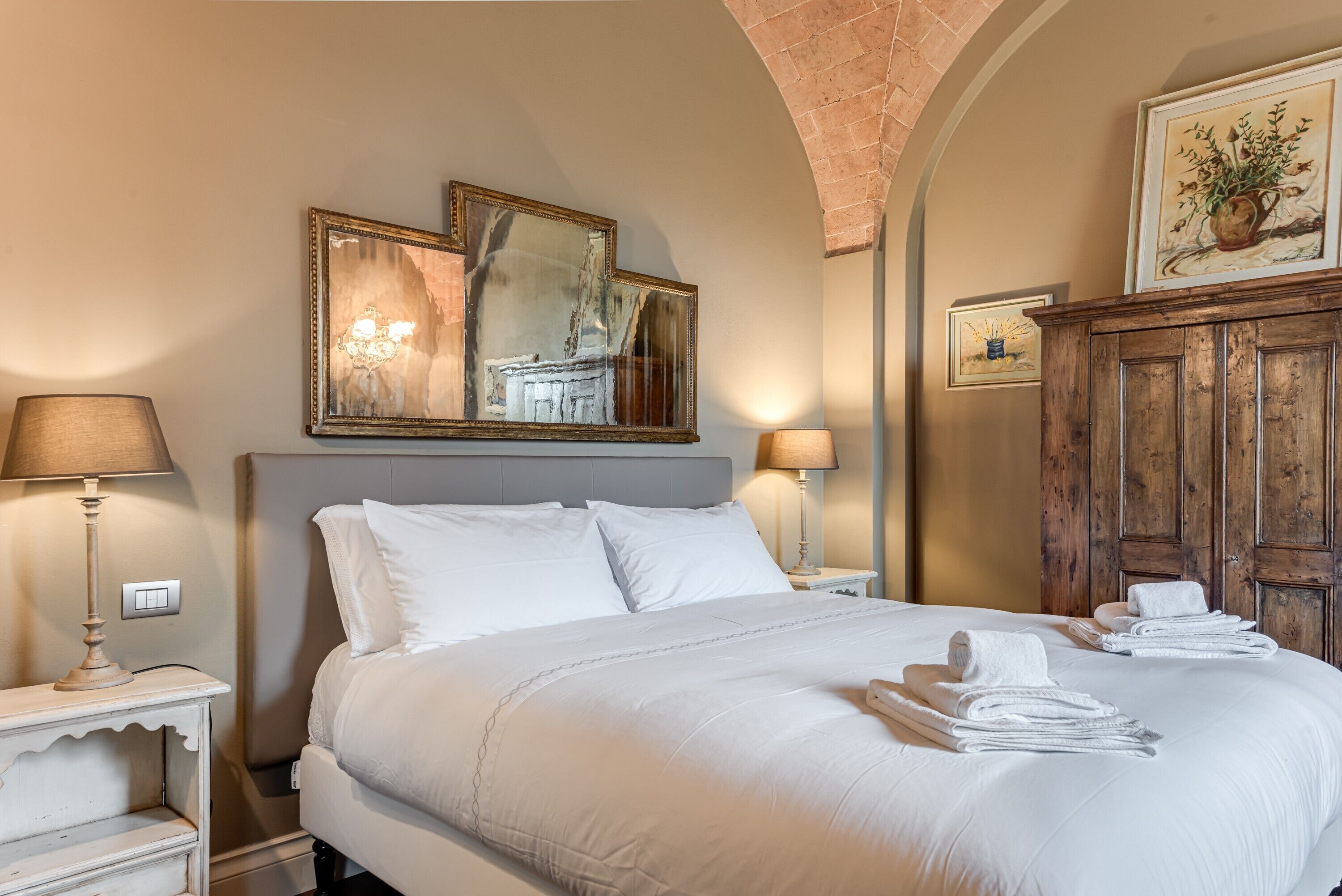Een hotelkamer met een groot bed, twee bedlampen, een houten kast en een spiegel aan de muur.