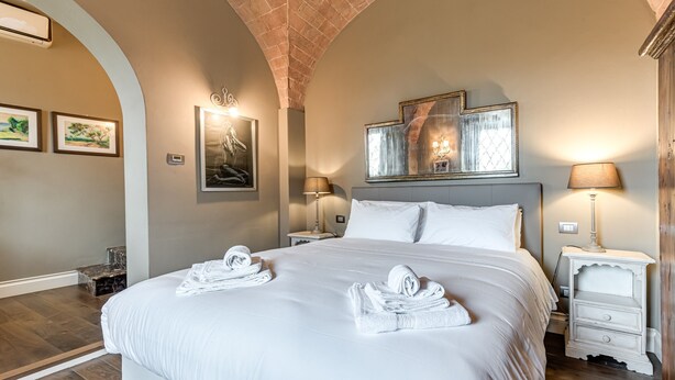 A hotel room with a large bed, two bedside tables, a nightstand, a brick ceiling, and framed artwork on the walls. - Room 'Pretty Suite Firenze' with Private Garden, Wi-Fi and Air Conditioning (Fiesole)