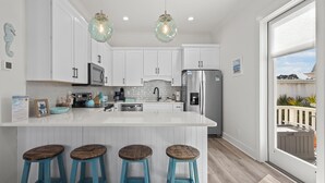 Una cocina moderna con armarios blancos, una isla grande con taburetes, electrodomésticos de acero inoxidable e iluminación colgante.