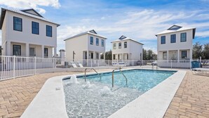 Una piscina con una fuente de agua, rodeada por una cerca blanca, y contigua a edificios blancos modernos.