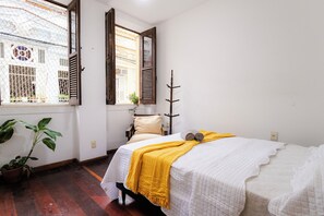 A bedroom with a bed, a window with shutters, a potted plant, and a wooden stick on the wall. - SUH Catete 06 Big House Metro (Rio de Janeiro)