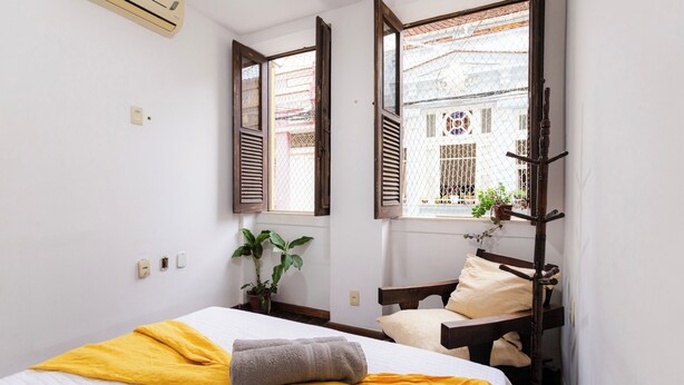 A bedroom with a bed, a window with shutters, a potted plant, and a wall-mounted air conditioner. - SUH Catete 06 Big House Metro (Rio de Janeiro)